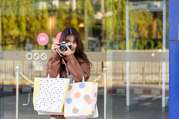 Shopping woman enjoys lifestyle fashion holds bags from black friday mall sales, people watch her posing with camera outside shop capturing fun holiday moments