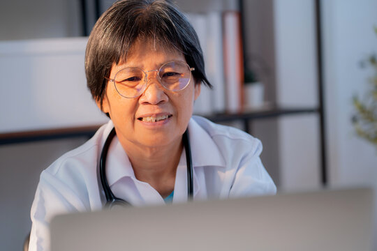 Senior asian doctor woman working on laptop computer on desk in clinic, elderly female physician video call or online consultation with medical, assistance or support with medical.