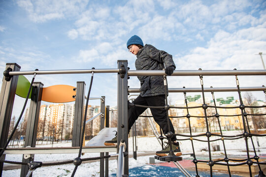 A child climbs on a modern outdoor playground structure in winter in an urban residential area.
