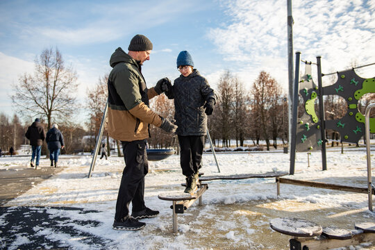 Father helping a child balance on playground stepping stones in a snowy park on a clear winter day, capturing a moment of outdoor play, trust and learning.