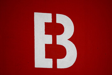 White letter B stencil sign split in half on a vibrant red background. Minimalist graphic typography detail and urban signage. © VladyslavShcherbakov