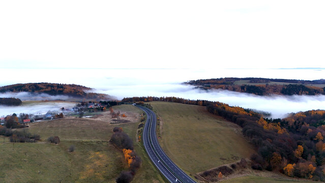 Aerial view of winding road through autumn hills with mist filling distant valleys, showing serene seasonal atmosphere, depth of landscape, and natural scenic harmony.
