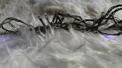 Close-up loop of colorful LED string lights glowing on a soft white fur surface, creating a cozy and festive ambience. Detailed illumination textures enhance the warm decorative atmosphere. - Powered by Adobe