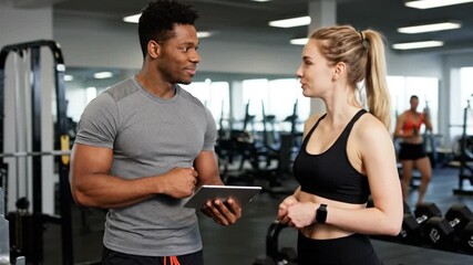 Supportive Personal Trainer and Client Discussing a Digital Fitness Plan on a Tablet in a Modern Gym