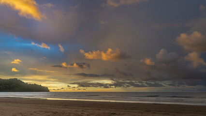Tropical sunset over the ocean. The blue sky is highlighted with golden at the horizon. Picturesque cumulus clouds. A hill in the distance. Sandy beach. Malaysia. Borneo. Kota Kinabalu.