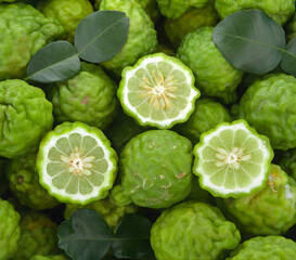 Fresh Kaffir Limes and Leaves Background, Top View of Bergamot Fruit Halved Showing Pulp, Thai Cuisine and Citrus Ingredient