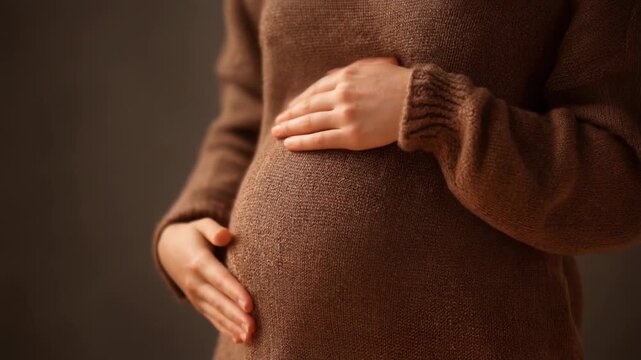 Embracing motherhood, a pregnant woman gently touching her baby bump in a cozy brown sweater