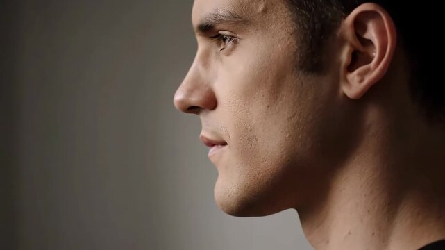 Young Man Profile - Close-up profile shot of a young man's face against a gray background. The man is facing left with a neutral expression.