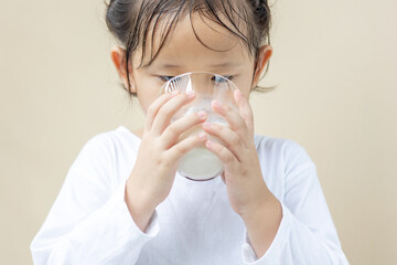 An Asian preschool girl holding a glass of milk.
