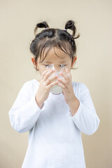 An Asian preschool girl holding a glass of milk.