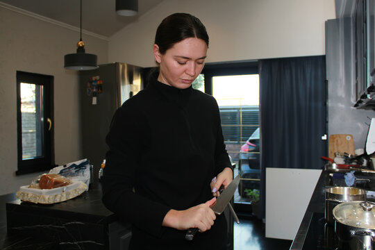 A woman at home, a woman's daily chores. Sharpening a knife with a steel, a woman sharpening a knife in the kitchen.