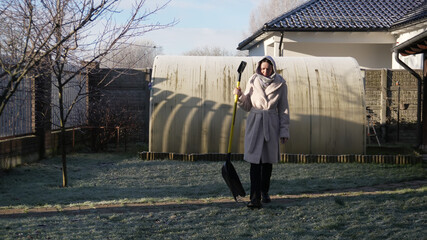  A woman's morning, working in the garden, daily chores. The woman is about to shovel snow with a wide shovel.