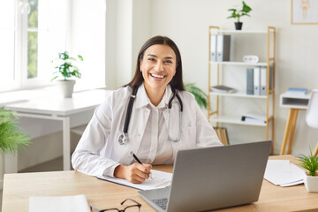 Portrait of a positive doctor or nurse working with a laptop in a hospital office. Healthcare...