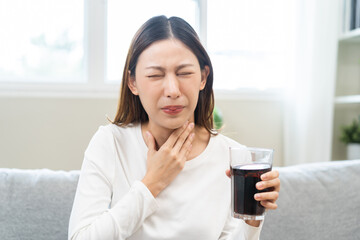 Acid reflux disease, suffer asian young woman, girl hand holding a glass of cola, have symptom gastroesophageal, heartburn pain on chest when drinking sparkling, soft water. Healthcare medical concept