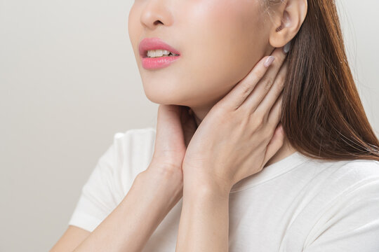 Sickness in inflaming asian young woman, girl use hand check self touch at sore throat, pain thyroid gland on neck or disease reflux, acid of suffer people on wall background. Medical and healthcare.
