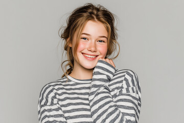 A smiling teenager with rosy cheeks and light brown hair modeling striped pajamas. Studio advertising portrait. Comfortable nightwear