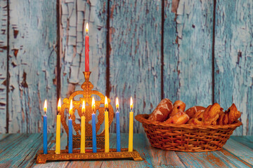 Menorah stands with lit candles beside basket of baked goods on wooden table, creating Hanukkah...