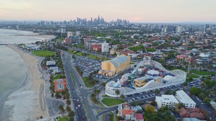 Fototapeta premium Panoramic Aerial View Captures Vibrant St Kilda Foreshore, Historic Luna Park, and Bustling Melbourne City Skyline at Dusk
