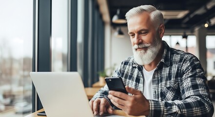 Senior man working with laptop and phone in bright cafe workspace.