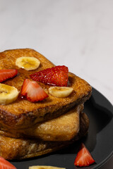 French toast breakfast with sliced strawberries and bananas on a plate topped with syrup – sweet homemade brunch food.