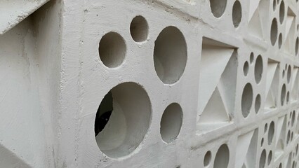 Detail of a cement roster wall with a repetitive pattern of circular and triangular holes.
