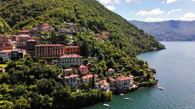 Scenic view of Nesso on Lago di Como, Italy, featuring hillside homes surrounded by dense greenery above calm blue water, with mountain slopes forming a peaceful lakeside setting under warm skies