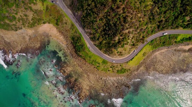 Top-down drone shot of Devils Corner on the Great Ocean Road with forest meeting the coastline and light traffic. Captures dramatic curves, blue ocean, green forest, and scenic coastal landscape.