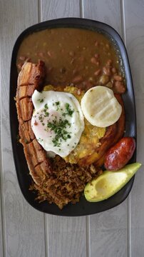 Close-up shot of Bandeja Paisa on a wooden table. Colombian dish with beans, rice, chicharr&oacute;n, egg, and arepa showcased beautifully in vertical video for mobile and social media.