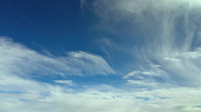 An aerial view of frayed and ghostly high-altitude cirrus clouds in a blue sky. Footage taken from a jet cockpit flying in the upper atmosphere