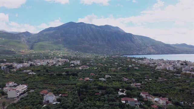 Aerial high angle view of eastern suburbs of Kalamata, flying over olive tree orchards, right pan revealing Taygetus mountain and Messinian gulf on a cloudy autumn day 4K