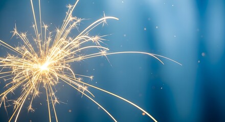 Golden sparkler igniting, creating a dazzling burst of light trails against a soft blue backdrop