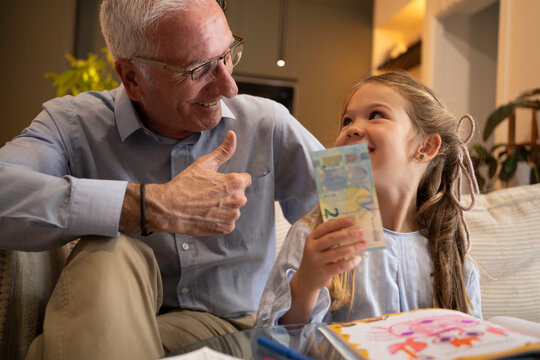 Grandfather giving money to his happy granddaughter making a thumbs up gesture