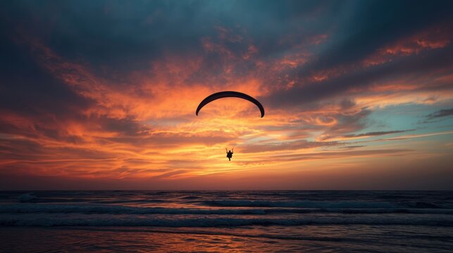 Paraglider silhouetted against a vibrant sunset over the ocean