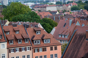 Rooftops of colorful buildings with red tiled roofs, surrounded by lush trees and distant cityscape, showcasing urban architecture and vibrant community life