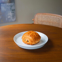 Fresh golden Pain au Chocolat on a white plate. Flaky French chocolate croissant pastry served on a wooden table