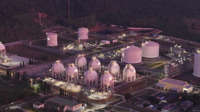 large oil tanker docked at a refinery terminal with multiple white storage tanks, complex pipeline networks, and offshore loading platforms.