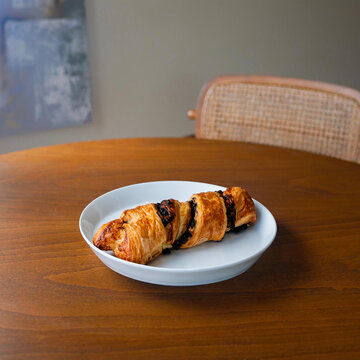 Golden chocolate twist pastry (Torsade) on a white plate. Fresh puff pastry with chocolate chips served on a wooden table