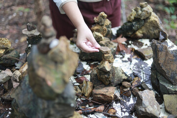 Calm child hand carefully stacking stone for balance and meditation in nature. peaceful moment of focus creating cairn art sculpture in forest setting