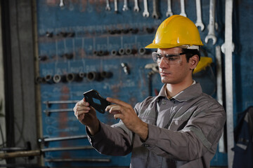 Factory welder metal worker inspects part under bright light in industrial workshop, focused and calm, wearing hard hat and safety glasses, precision quality control in manufacturing environment