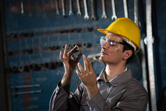 Factory welder checks metal part with focused worker workshop tool wall backdrop wearing hard hat and safety glasses for precision quality control industrial setting with calm determination