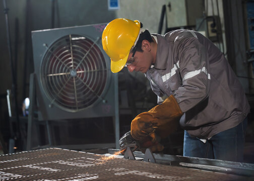 Factory welder metal worker sparks grind steel grate in industrial workshop with focus and care under yellow helmet and glove protection by machine tool - Powered by Adobe