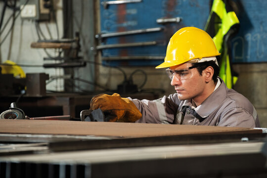 Industrial factory welder focused on metal fabrication, skilled worker with hard hat and gloves near workshop table, sparks in air, determined mood under warm light and rugged texture background