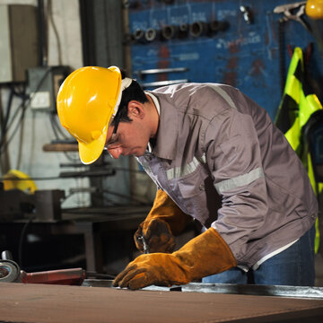 Factory welder metal worker in safety helmet and glove focuses on precise cutting on steel table in workshop, sparks fly with gritty mood and strong light, industrial craft and skill show in action