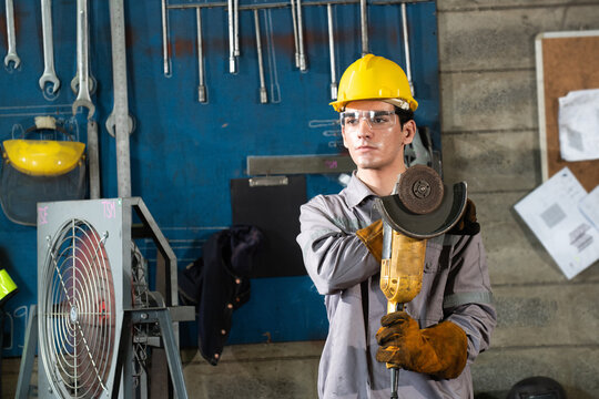 Factory welder metal worker hard hat holds angle grinder with focus and determination industrial workshop, sparks feel near, safety glove and goggle show care, concrete wall and tool rack frame - Powered by Adobe