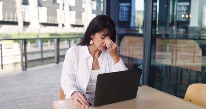 Stress, woman and headache with laptop at cafe for creative workload, author pressure or remote work. Freelance editor, mature person or tech with migraine at outdoor coffee shop for editing overload