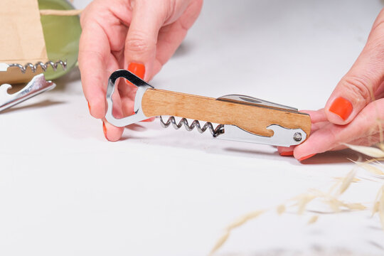 wooden bottle opener, corcscrew with switchblade in woman hands on white background, commercial photo concept