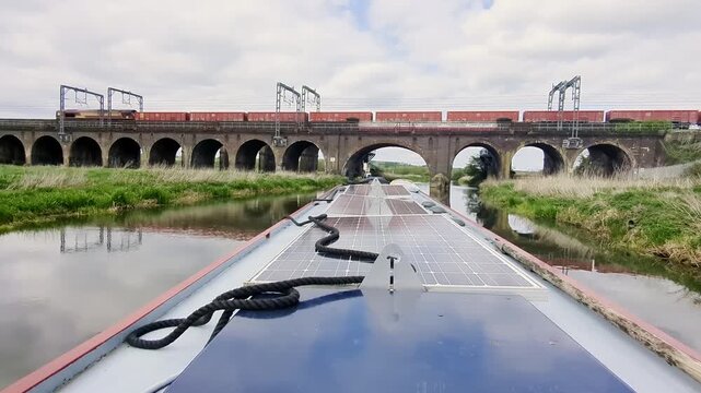 View from a narrowboat cruising towards a railway viaduct across the river Nene in Northamptonshire just as a freight train passes across the bridge. No logos visible.