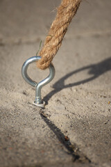 Galvanized eye bolt (hook), fixed into a concrete or ground surface, with a thick rope knotted through it.