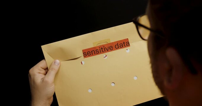 A worker carefully seals a brown envelope labeled &ldquo;sensitive data,&rdquo; symbolizing data protection and confidentiality in the workplace.