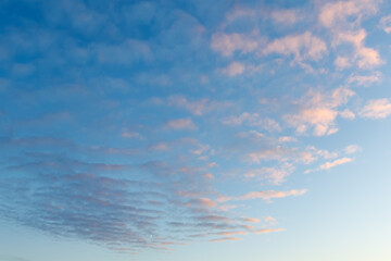 The sky is filled with delicate pastel clouds at dawn or sunset. Pink and purple hues contrast softly against the blue sky. A small crescent moon is visible near the horizon.